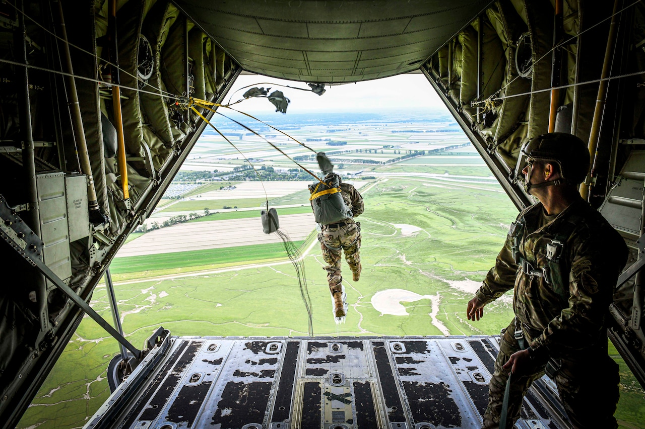 A special forces member jumps from the back of an aircraft into the fields below while another watches on from the aircraft.