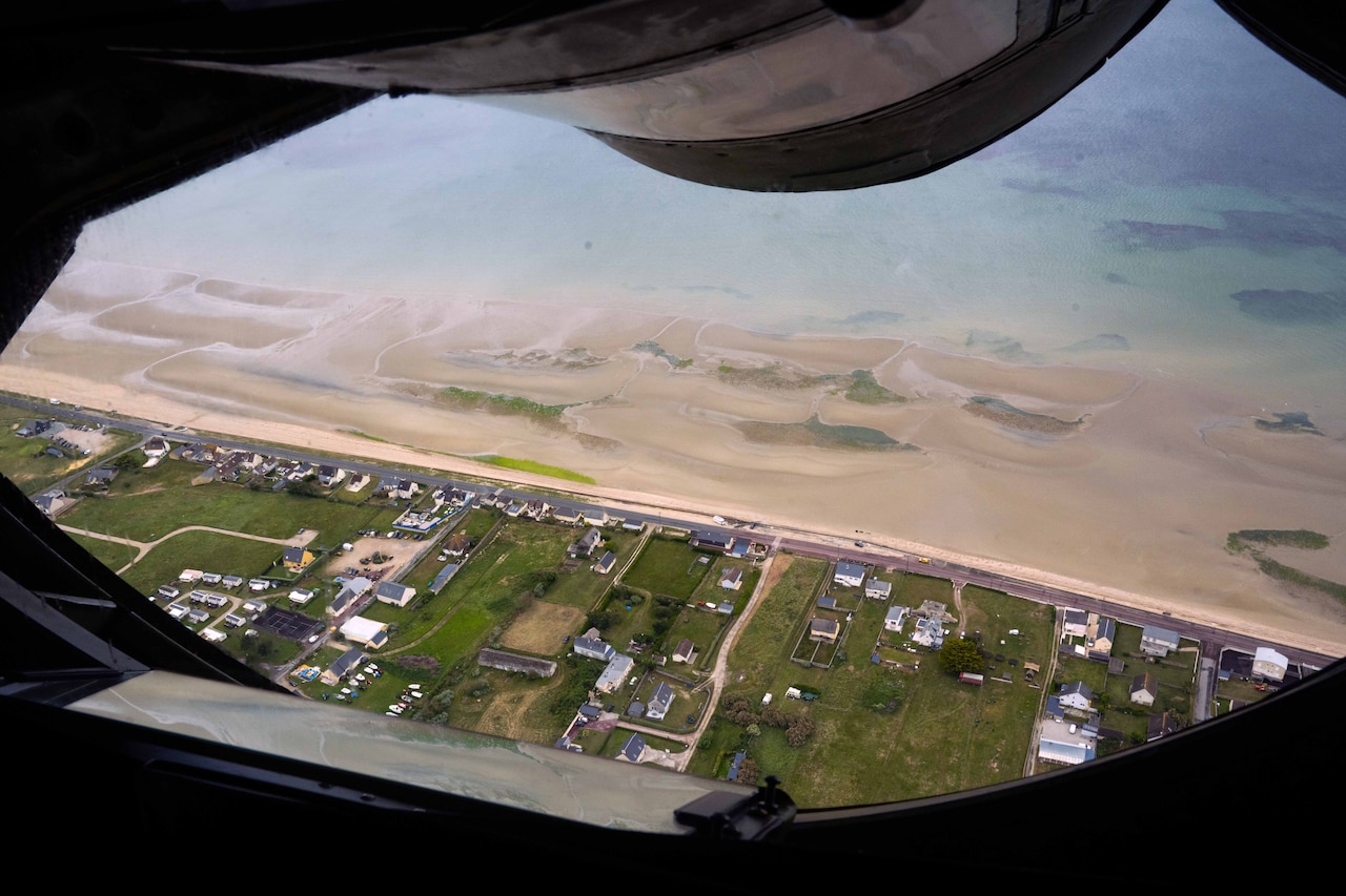 From the window of an aircraft, a houses are seen along a beach.
