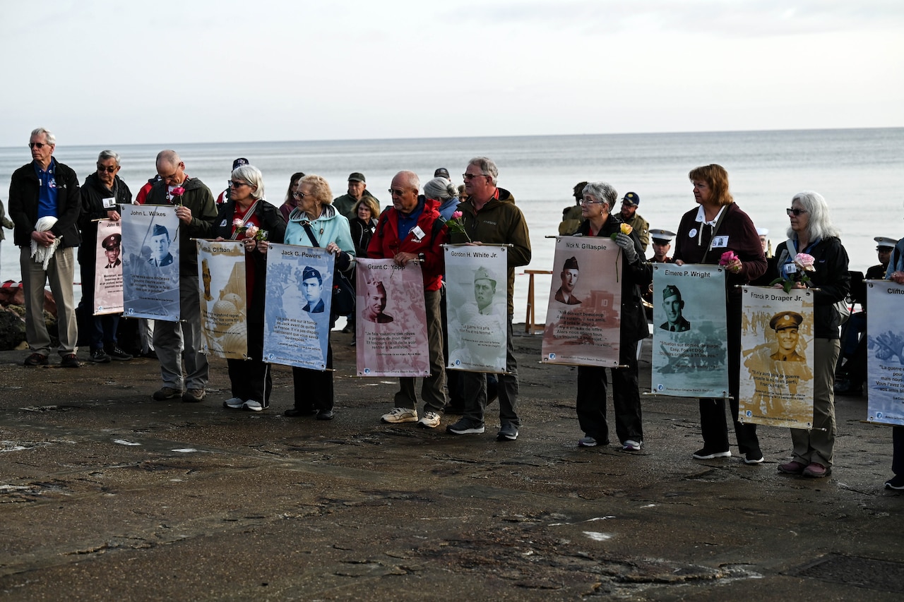 A group of people stand in a line holding banners with faces of World War II service members.
