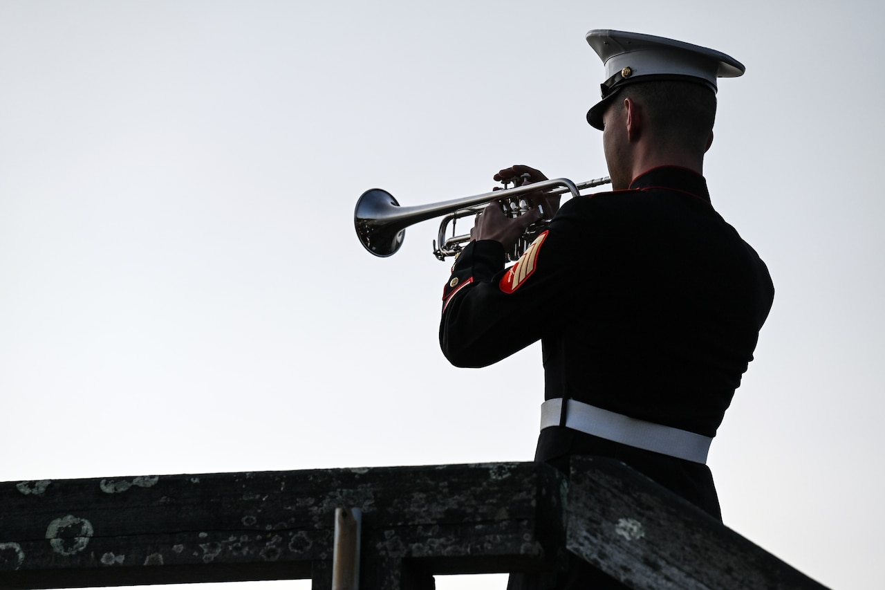 The back of a bugler is shown playing in front of a wide sky.
