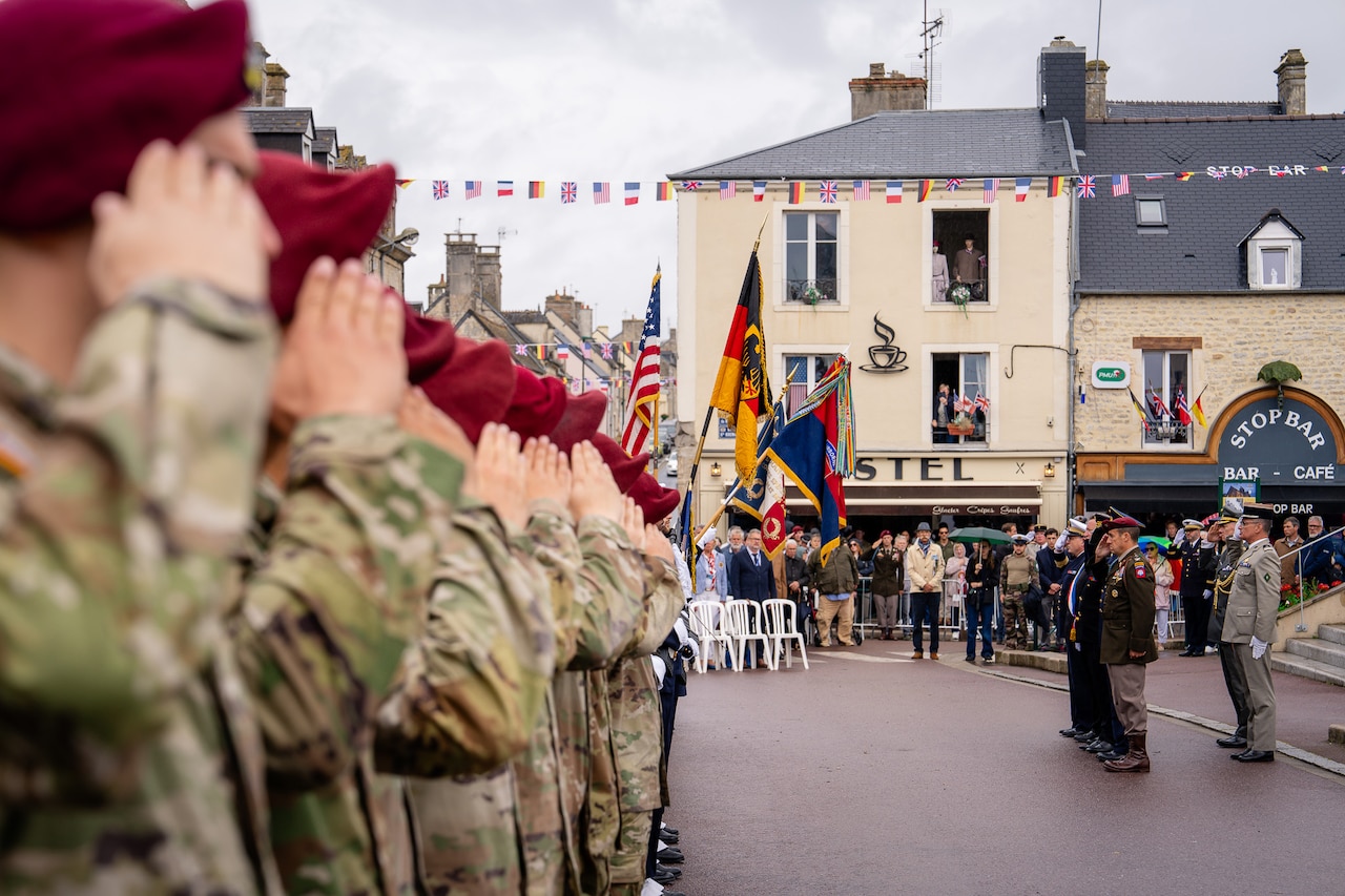 U.S. service members salute at a town square during an overcast day.