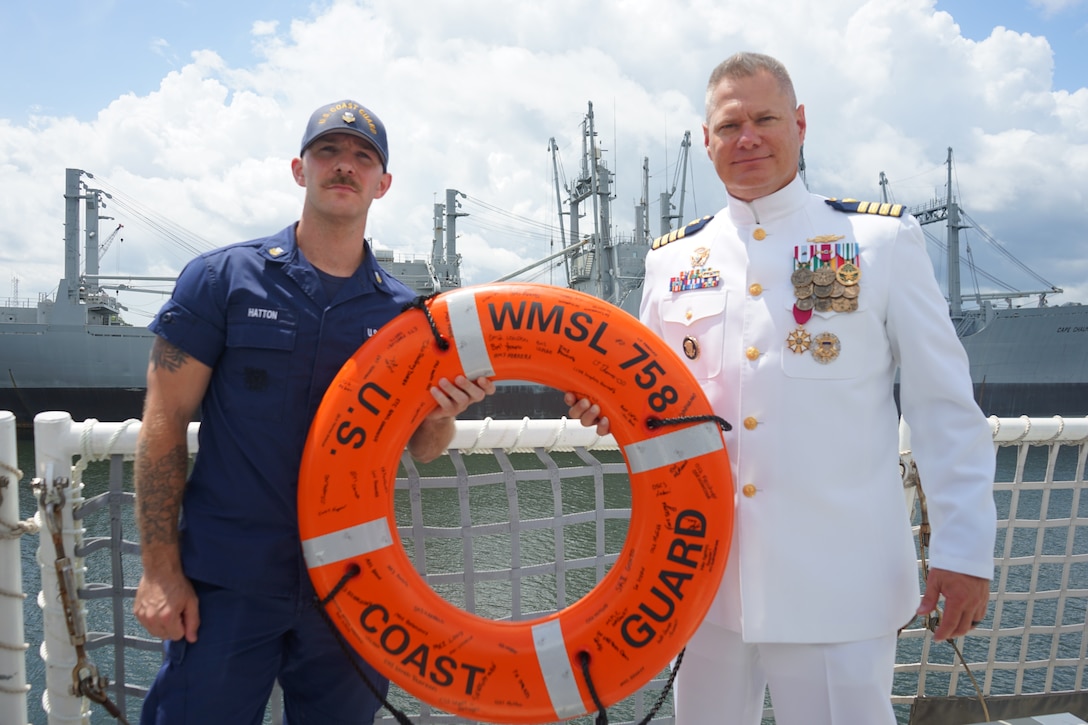 Capt. Jonathan Carter, commanding officer of Coast Guard Cutter Stone (WMSL 758), and Petty Officer 1st Class Lucas Hatton, a crew member assigned to Stone, pose for a photo with Carter's going away gift following the cutter's change-of-command ceremony in North Charleston, South Carolina, June 5, 2025. The change-of-command ceremony is a time-honored tradition that formally demonstrates the continuity of authority within a command, conducted before the assembled crew and honored guests. (U.S. Coast Guard photo by Ensign Sarah Pearson)