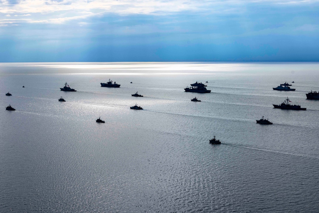 Multiple vessels cruise in a calm sea with a blue sky in the background.