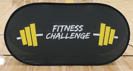 A “Fitness Challenge” banner stands at center court during a U.S. Army Fitness Challenge event at a Kansas City-area high school, May 2025. The challenge promotes physical fitness, teamwork, and Army values among high school students.
