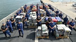 USCGC Valiant (WMEC 621) crew members pause for a group photo with pallets of drugs before offloading at Port Everglades in Fort Lauderdale, Florida, June 6, 2025. The Valiant crew offloaded more than $132 million in illicit drugs interdicted in the Caribbean Sea. (U.S. Coast Guard photo by Petty Officer 1st Class Diana Sherbs)