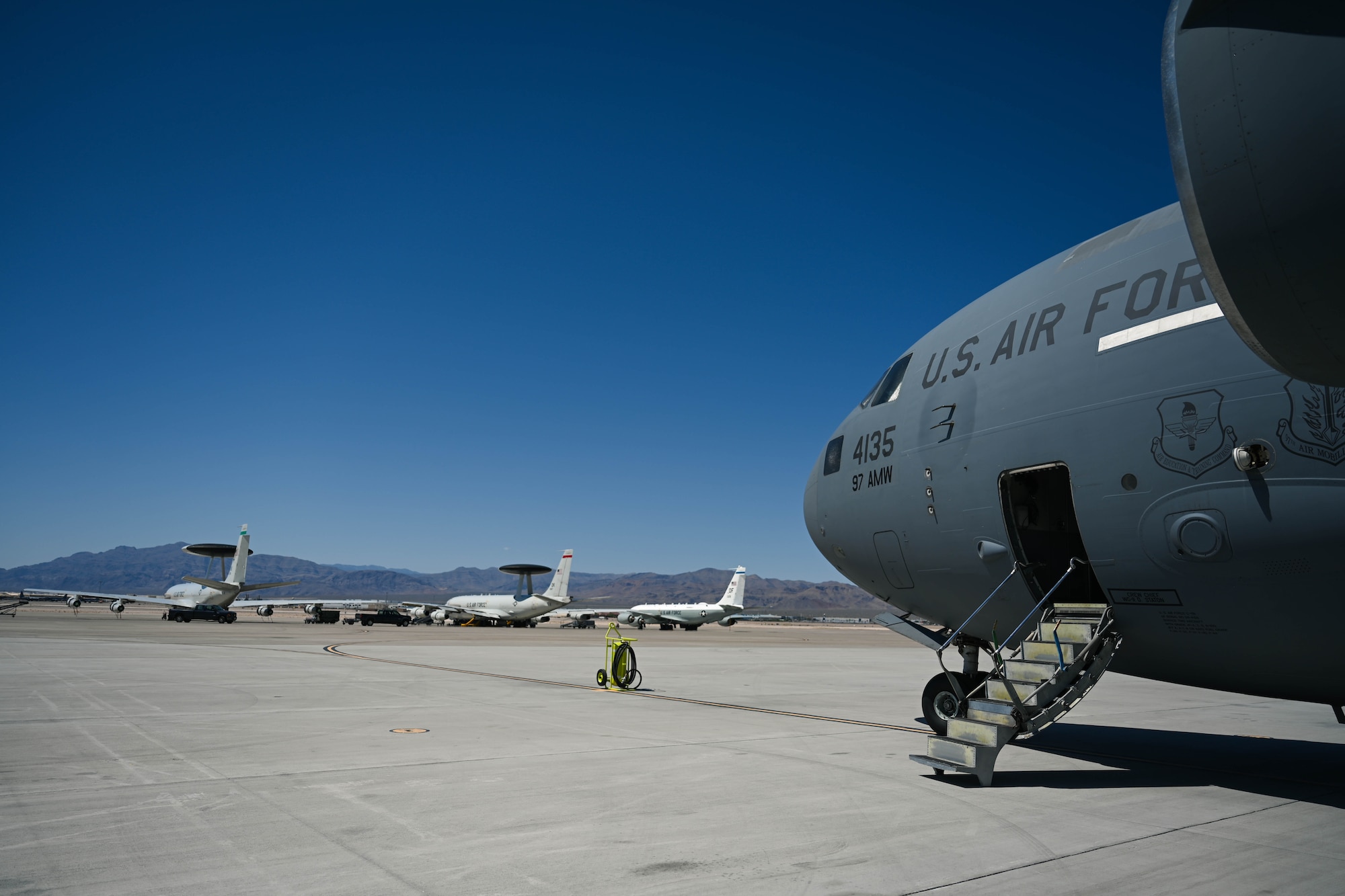 From right to left, a U.S. Air Force C-17 Globemaster III assigned to the 97th Air Mobility Wing, a RC-135 Rivet Joint assigned to the 55th Wing, and two E-3 Sentry aircraft assigned to the 552nd Air Control Wing are parked on the flightline at Nellis Air Force Base, Nevada, May 28, 2025. The aircraft were involved in a Joint Forcible Entry training sortie in support of the 57th Weapons Squadron course curriculum. (U.S. Air Force photo by Airman 1st Class Jonah Bliss)