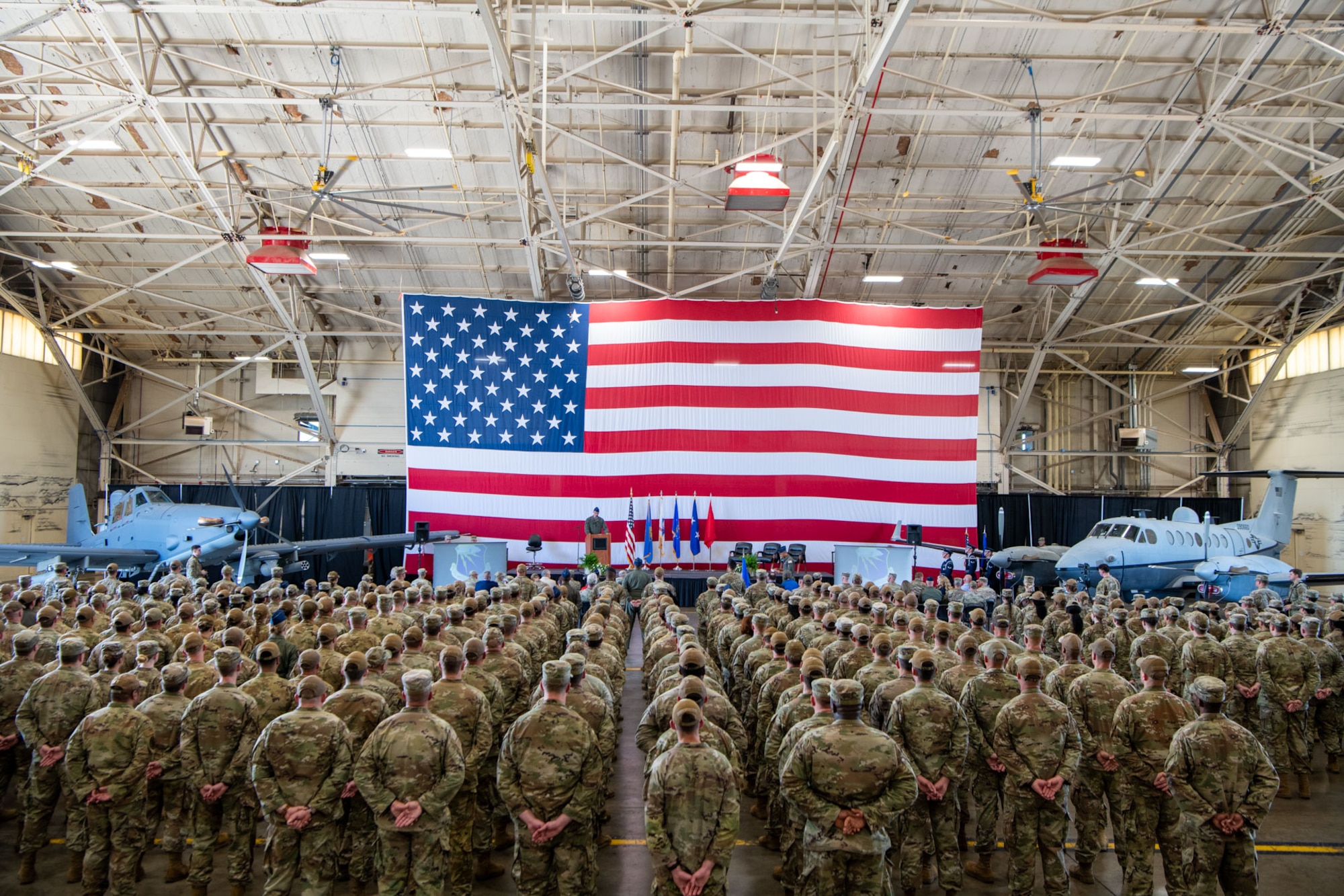 A group of Airmen stand in formation in front of an American flag and two aircraft