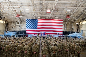 A group of Airmen stand in formation in front of an American flag and two aircraft