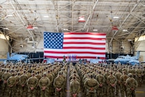 A group of Airmen stand in formation in front of an American flag and two aircraft