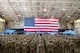 A group of Airmen stand in formation in front of an American flag and two aircraft