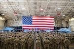 A group of Airmen stand in formation in front of an American flag and two aircraft