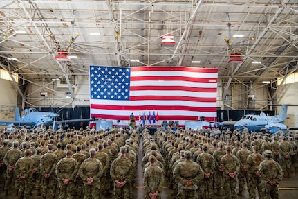 A group of Airmen stand in formation in front of an American flag and two aircraft