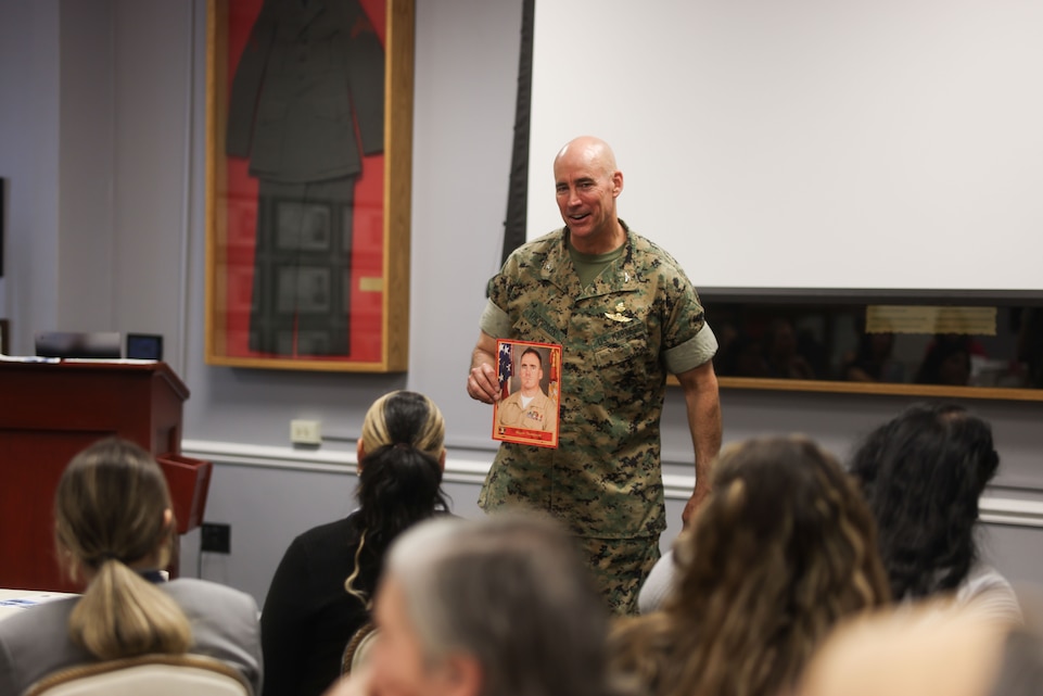 U.S. Marine Corps Col. Eric Thompson, Chief of Staff, II Marine Expeditionary Force, shows military spouses a picture of himself as a former Deployment Readiness Coordinator during the Camp Lejeune Leadership Seminar at Paradise Point Officers’ Club on Marine Corps Base Camp Lejeune, North Carolina, May 7, 2025. Thompson emphasized the significance of civilian affairs highlighting the role of civilians in sustaining the well-being of service members across the Marine Air-Ground Task Force. (U.S. Marine Corps photo by Lance Cpl. Caroline Perkins)