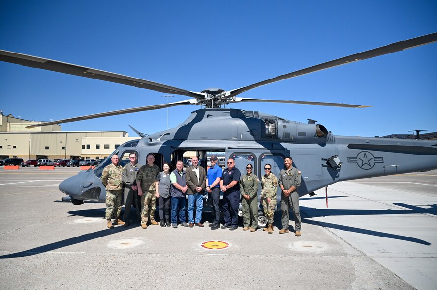 Airmen and civilians pose in front of an MH-139A helicopter