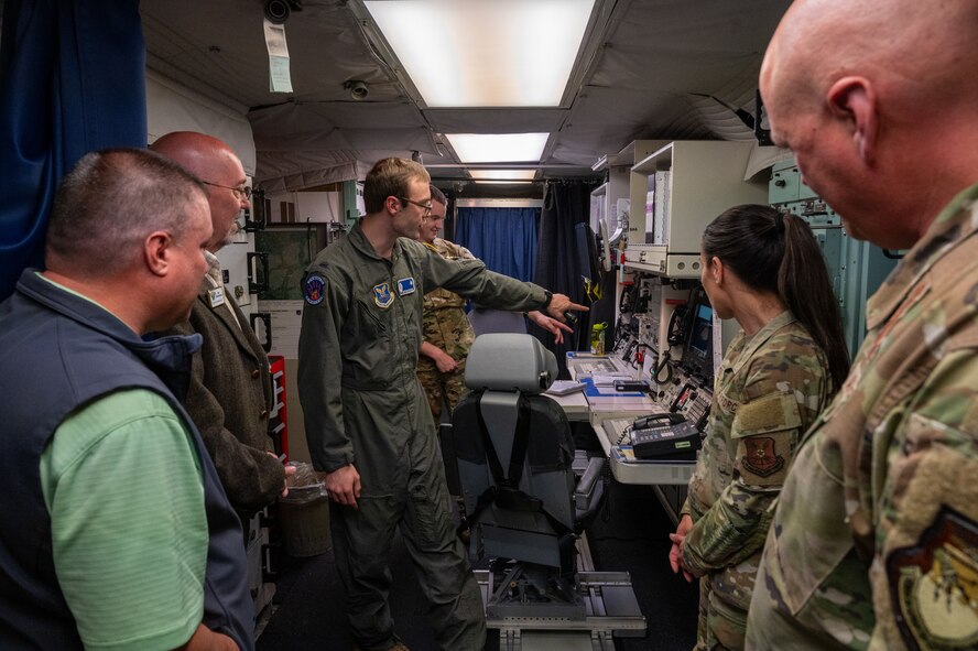 Two Missileers point at a launch console while two civilians and two Airmen watch