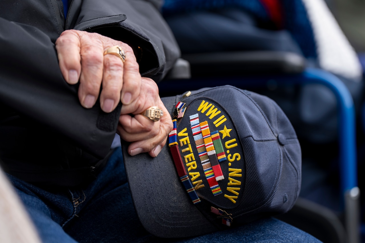 A seated person wearing two rings holds a hat.