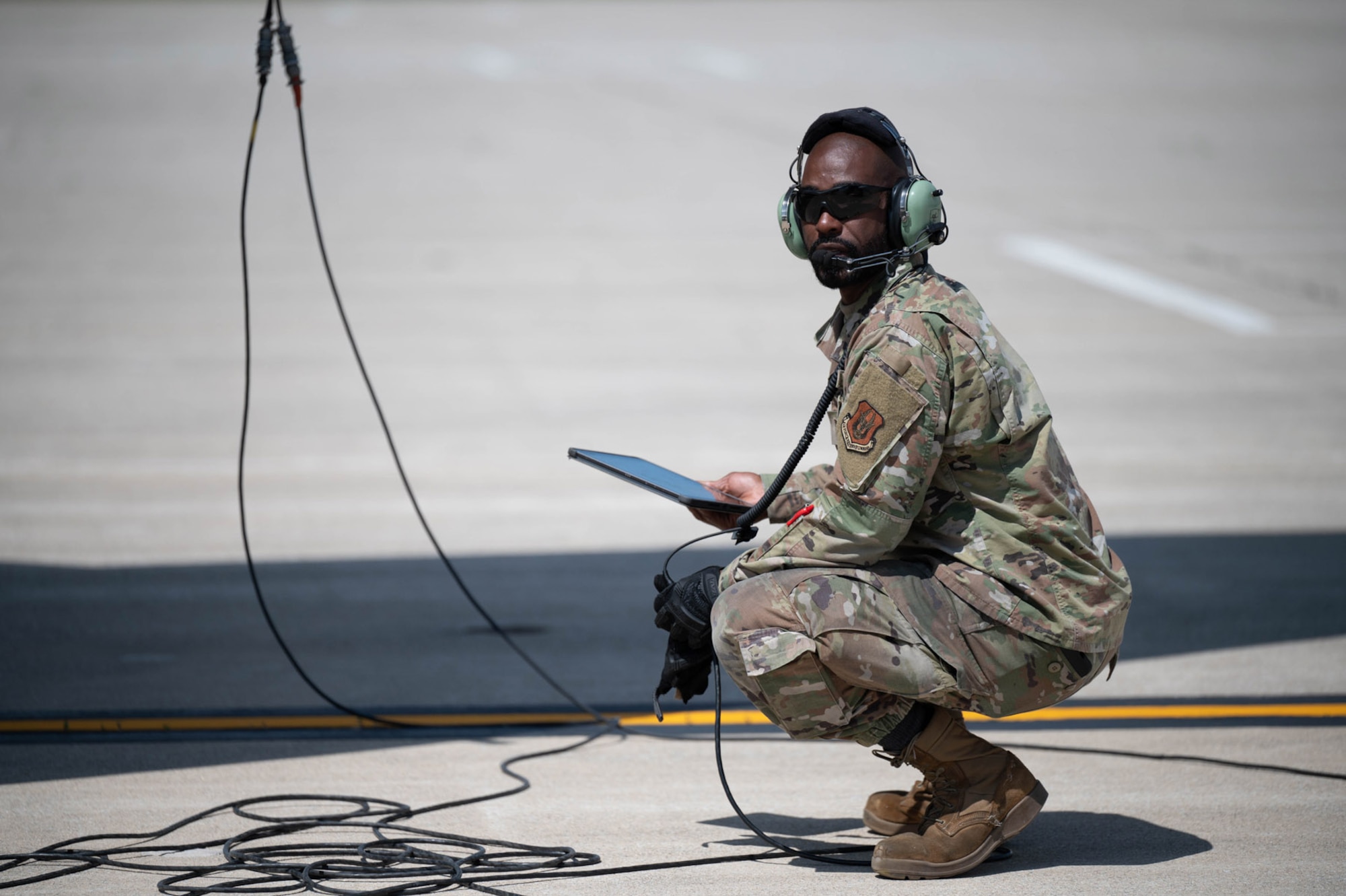 Crew chief crouches on the tarmac with a tablet in hand and headset on his head