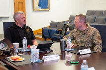A civilian and an Airman sitting at a table talking to each other