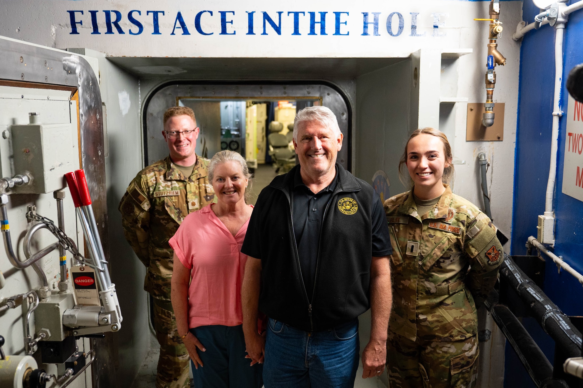 Two civilians and two Airmen stand in front of a vault door
