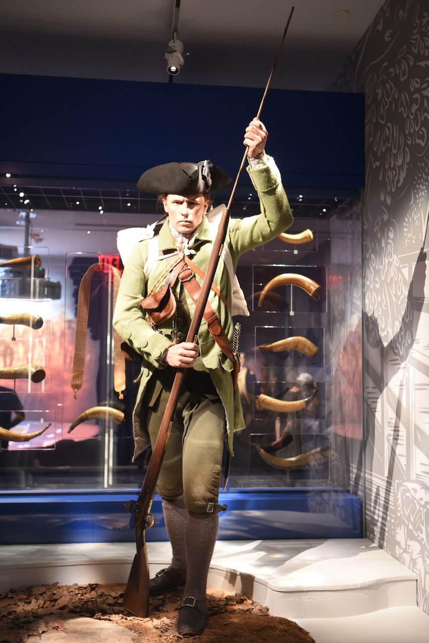 A mannequin dressed in a Continental Army uniform from the Revolutionary War is shown loading a musket inside a museum.