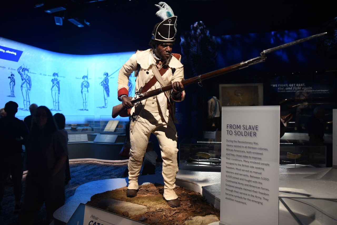 A mannequin in a Continental Army uniform is shown holding a rifle while on display at a museum.