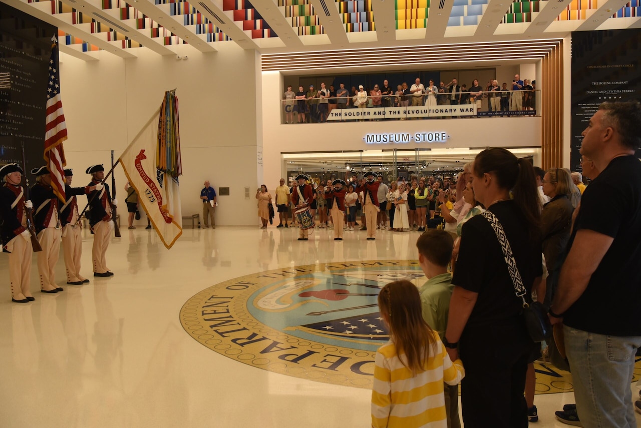 People wearing civilian attire watch military band members in historical Army uniforms perform at a museum.