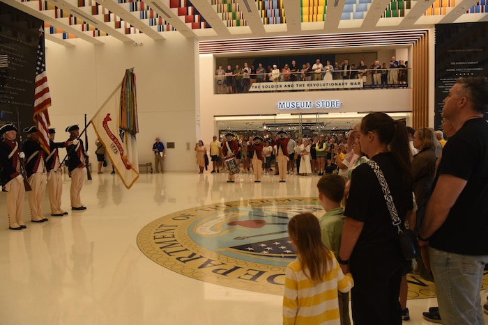 People wearing civilian attire watch military band members in historical Army uniforms perform at a museum.