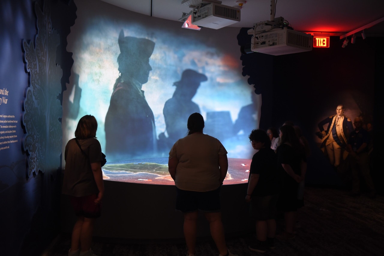 People in civilian attire view an interactive display at a museum.
