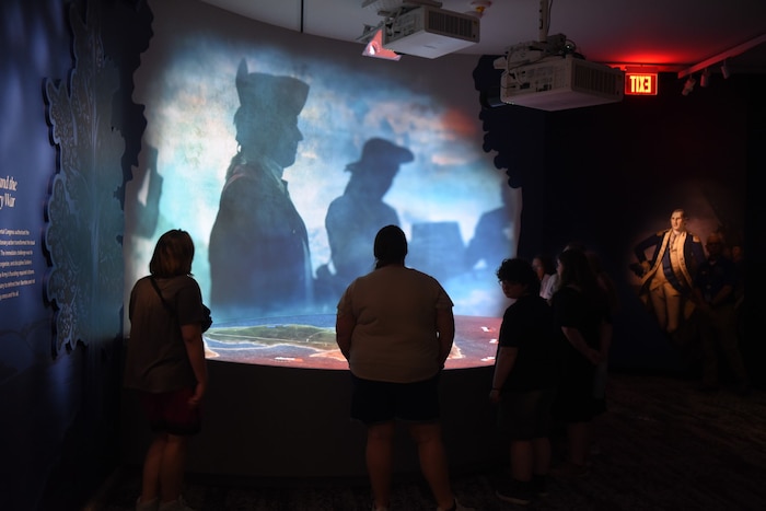 People in civilian attire view an interactive display at a museum.