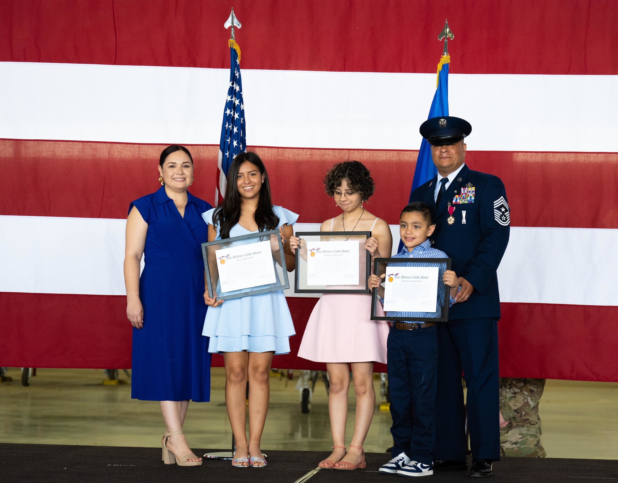 Esmerelda Largaespada, left, and Chief Master Sgt. Lester Largaespada, right, 47th Flying Training Wing command chief, present the Military Child Medal to his three children at Laughlin Air Force Base, Texas, June 6, 2025. The retirement ceremony celebrated the 29 year career of Largaespada. (U.S. Air Force photo by Staff Sgt. Nicholas Larsen)