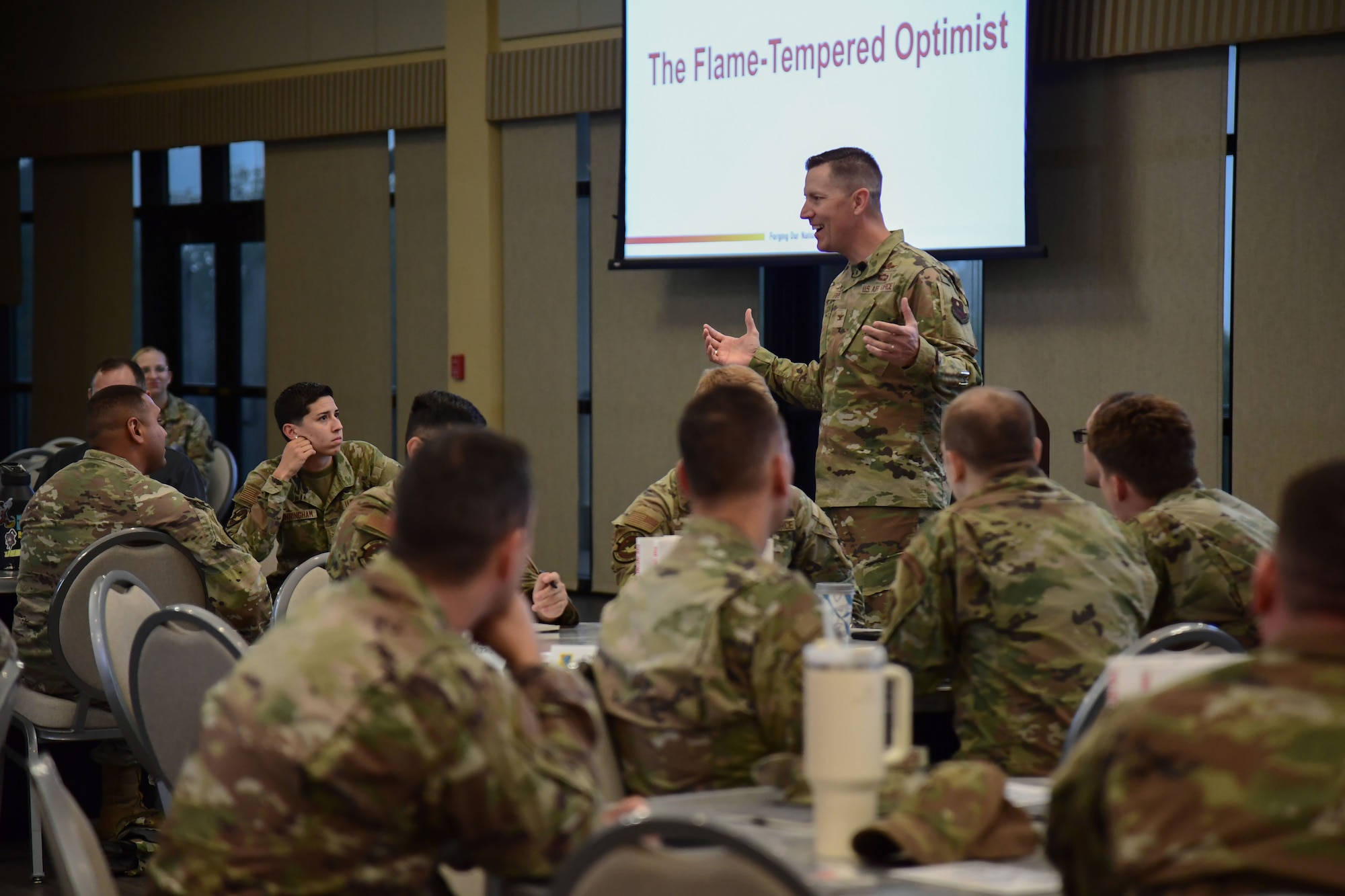 A room full of service members listen a an Air Force officer speaking.