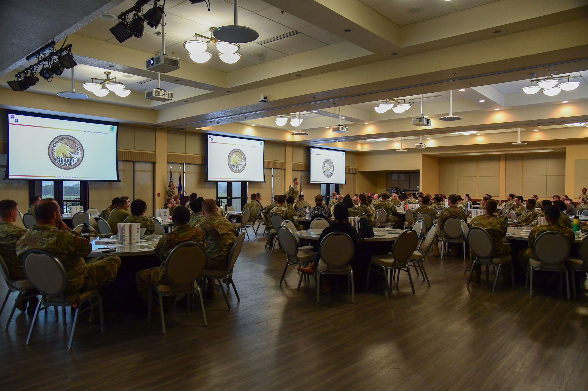 A room full of service members listen to an Air Force officer speak.