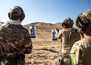 U.S. and Chilean service members practice aiming at a wooden board with a photo on it in the middle of a desert