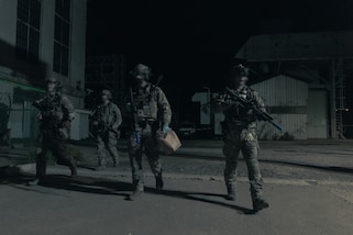 Service members carrying weapons and a paper bag walk out of a powerplant after a training