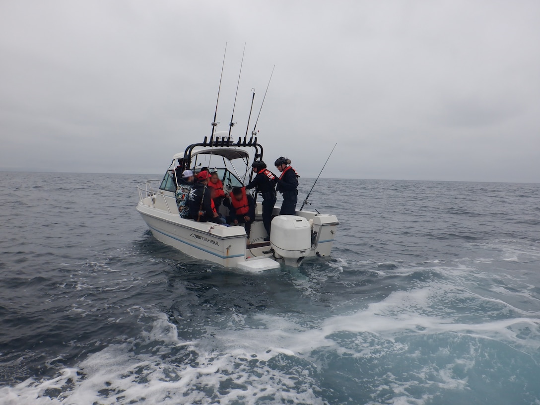 Coast Guardsmen talk to Mexican migrants aboard a white boat with fishing poles on the Pacific Ocean.