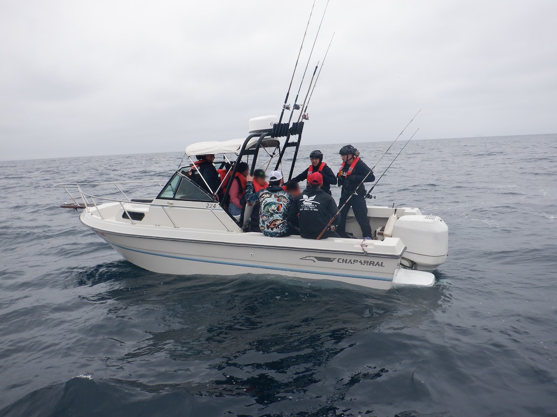 Coast Guardsmen talk to Mexican migrants aboard a white boat with fishing poles on the Pacific Ocean.