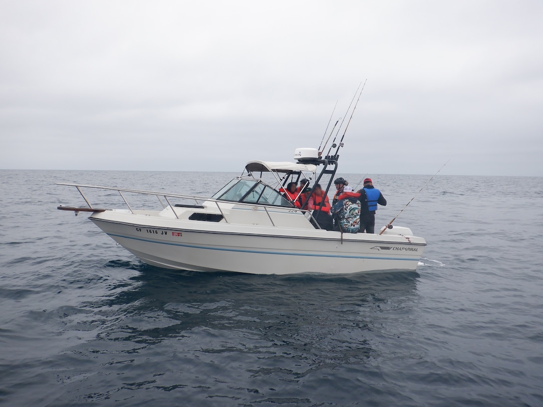 Coast Guardsmen talk to Mexican migrants aboard a white boat with fishing poles on the Pacific Ocean.