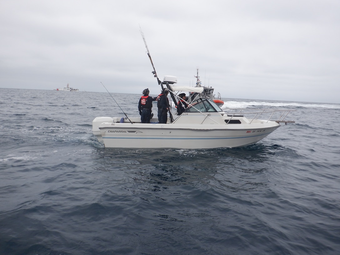 Coast Guardsmen talk to Mexican migrants aboard a white boat with fishing poles on the Pacific Ocean.