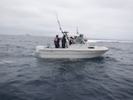 Coast Guardsmen talk to Mexican migrants aboard a white boat with fishing poles on the Pacific Ocean.