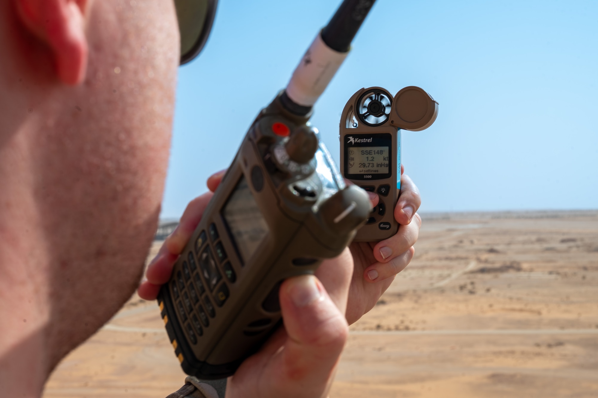 Airman holds a weather device and a radio on the catwalk of an ATC tower