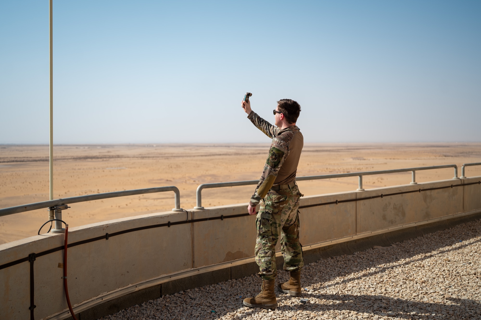 Airman stands on the catwalk of an ATC tower and holds a weather device