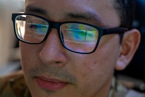 The reflection of an Airman's glasses shows a weather map on a computer screen.