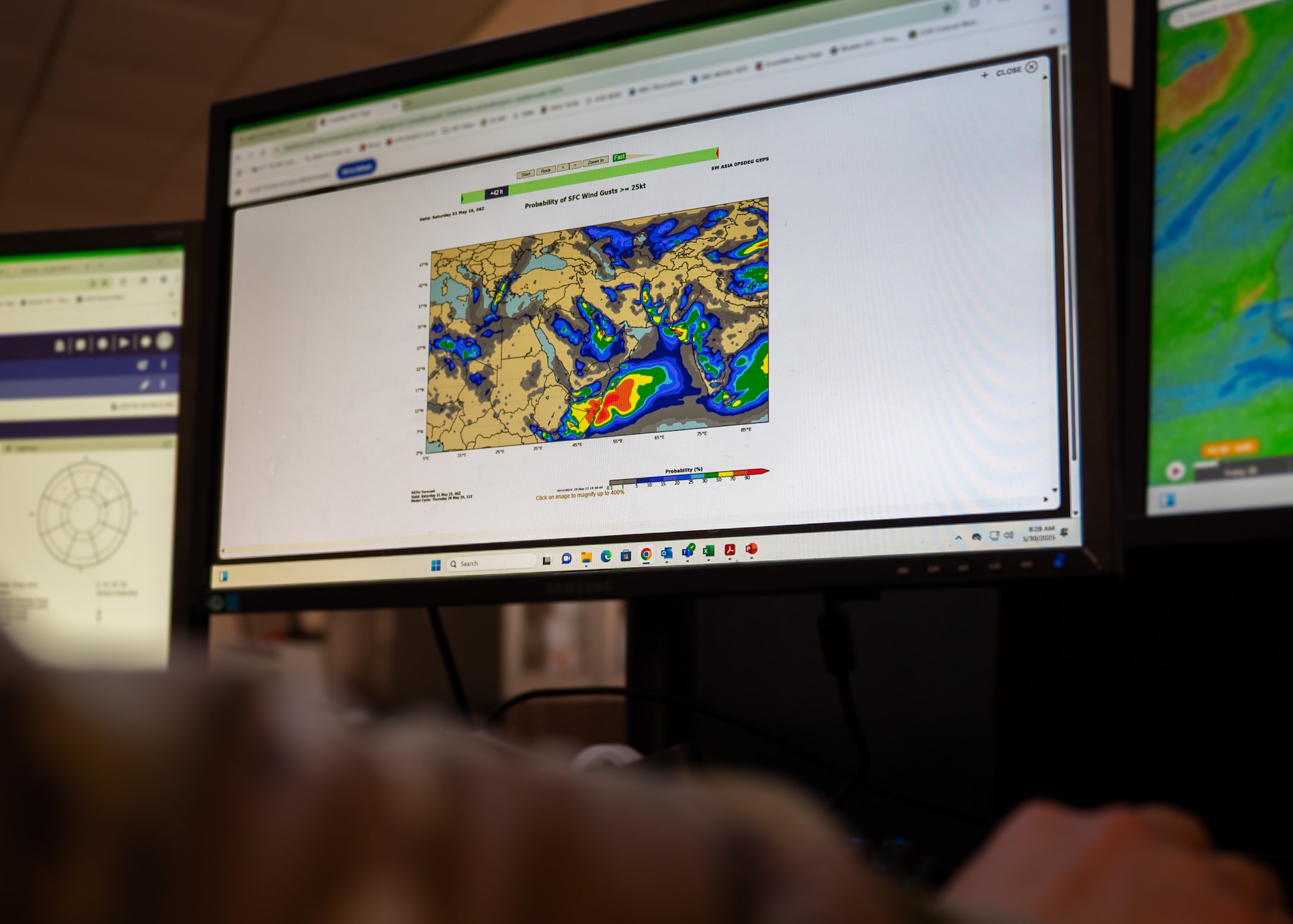 Airman holds their hand on a computer mouse while looking at a weather map on a computer screen