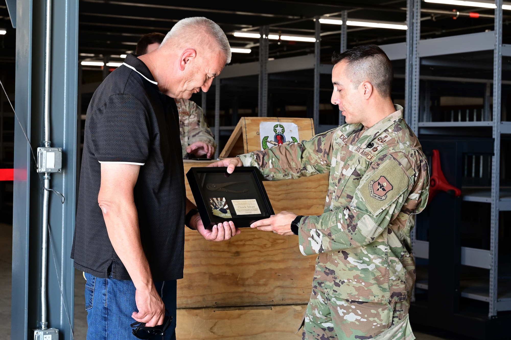944th Fighter Wing Engineering Technician, Mr. Chuck Tehan 
accepts a plaque from Chief Master Sgt. Carlos Sanchez, 56th Civil Engineer Squadron Explosive Ordnance Disposal flight chief, at the EOD Ribbon Cutting Ceremony for their new mezzanine at Luke Air Force Base, Ariz., June 3, 2025. Tehan was instrumental is the new facility being funded and followed up regularly to make sure timelines and needs were being met. (U.S. Air Force Photo by MSgt Courtney Richardson)