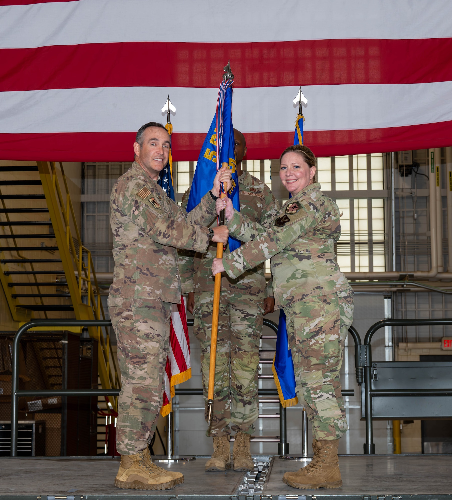 U.S. Air Force Col. Jesse Lamarand, 5th Bomb Wing commander, presents Col.. Tiffany Arnold, 5th Maintenance Group (5MXG) commander, the guidon during the 5MXG change of command ceremony at Minot Air Force Base, North Dakota, June 4, 2025. The passing of the guidon represents Arnold’s assumption of command of the 5MXG. (U.S. Air Force photo by Senior Airman Alex Nottingham)