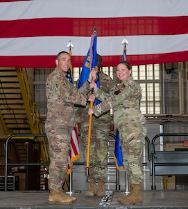 U.S. Air Force Col. Jesse Lamarand, 5th Bomb Wing commander, presents Col.. Tiffany Arnold, 5th Maintenance Group (5MXG) commander, the guidon during the 5MXG change of command ceremony at Minot Air Force Base, North Dakota, June 4, 2025. The passing of the guidon represents Arnold’s assumption of command of the 5MXG. (U.S. Air Force photo by Senior Airman Alex Nottingham)