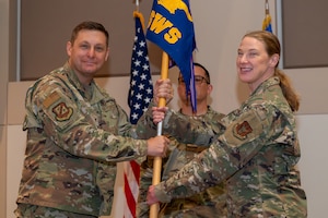 Two people in miliary uniforms holding a flag.