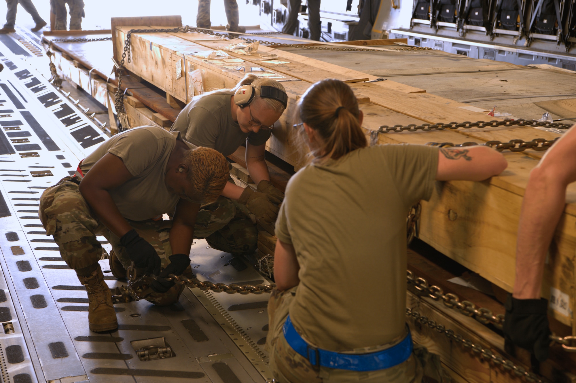 73rd Aerial Port Squadron Airman, AMN Danielle Cook observes a 60th Aerial Port Squadron Airman fastens a chain to secure a palletized cargo crate inside a C-17 Globemaster III during annual tour training at Travis Air Force Base, Calif., April 14, 2025. The training supports the development of multi-capable Airmen across aerial port specialties.
