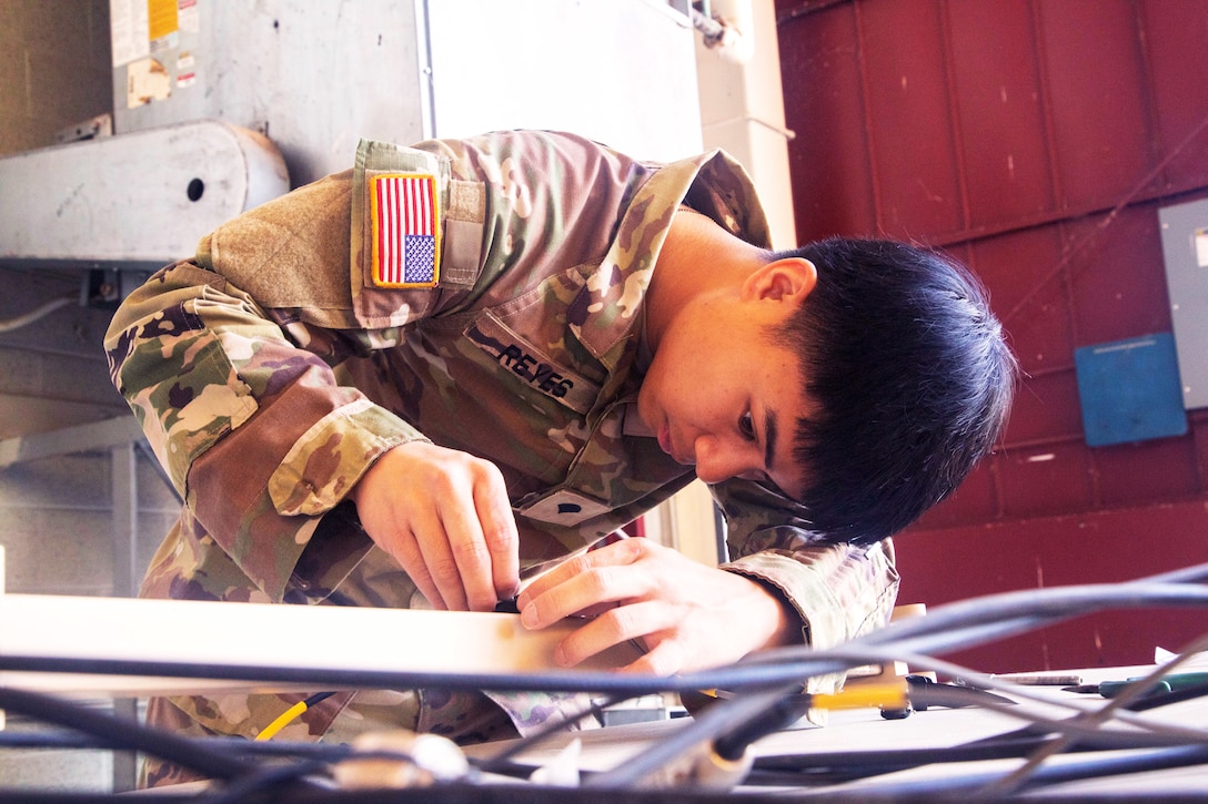 A soldier replaces components on a piece of electrical equipment by hand.