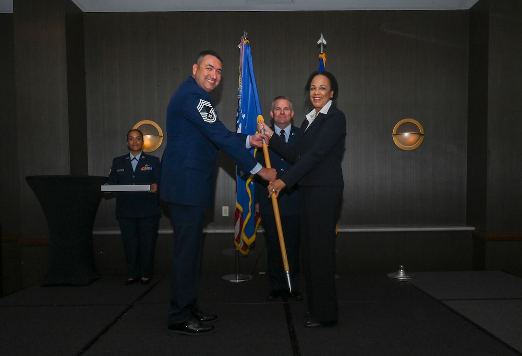 Chief Master Sgt. Samuel Strawbridge, 356th Airlift Squadron senior leader, hands the 433rd Airlift Wing guidon to Michelle Hoskins, Reaching Maximum Independence president, during the 433rd AW 2025 Honorary Commanders’ Induction Ceremony in San Antonio, June 7, 2025.